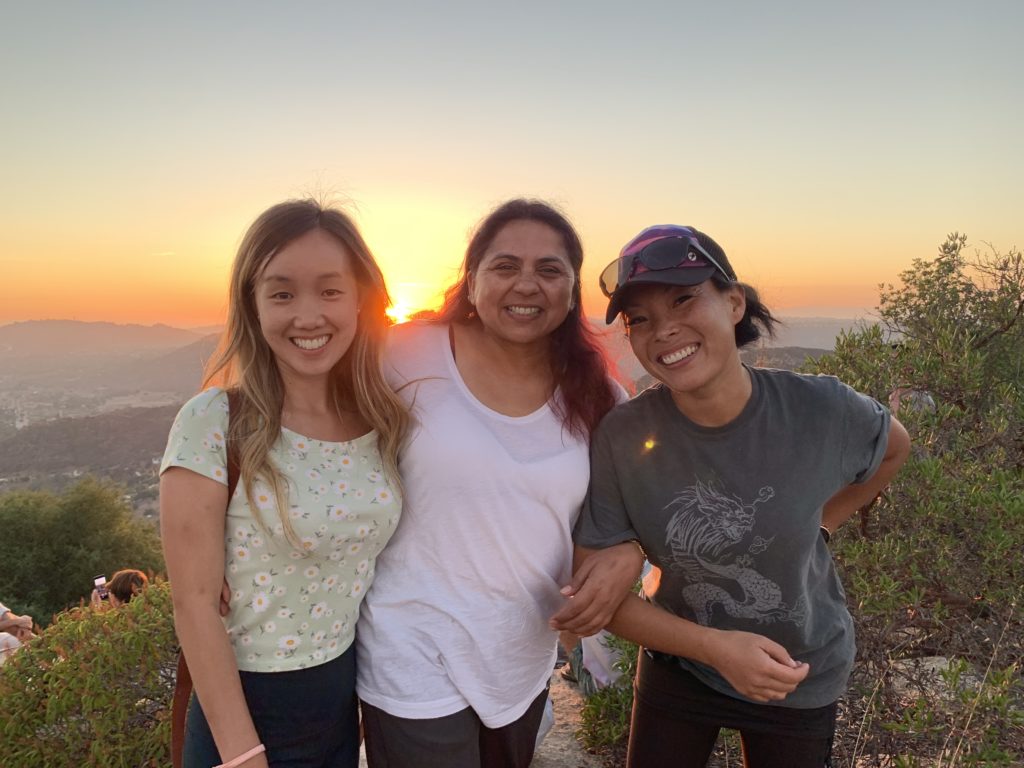 Three women smiling with the sunset behind them.